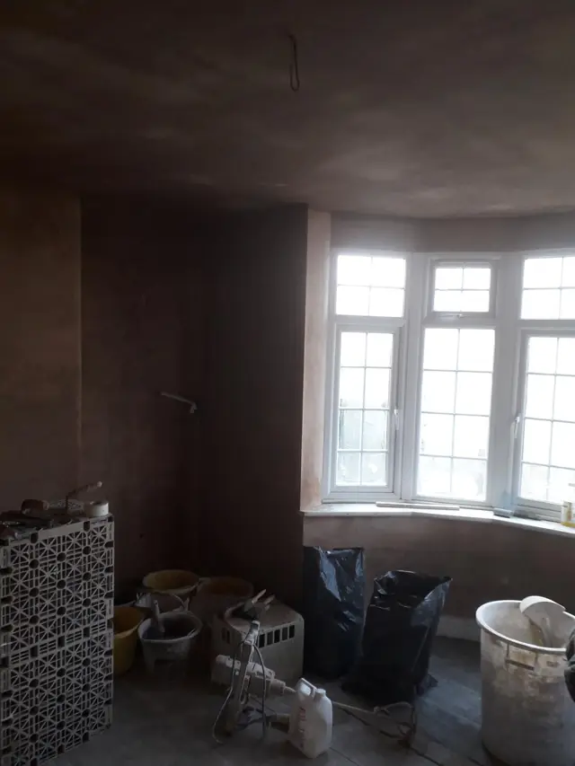 Bay-windowed room in Great Missenden newly floated and set, the fresh plaster still drying, with buckets and tools on the floor