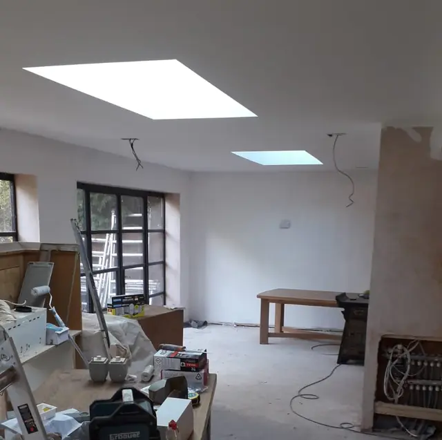 Open-plan room with freshly plastered walls and ceiling, three roof lights and a kitchen part-way through being fitted
