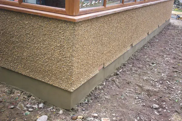 Corner of a building with a new pebble dash finish above a smooth render plinth