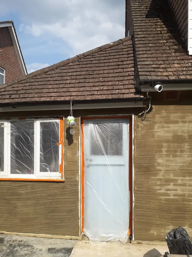 Sand and cement scratch coat on a single-storey extension in Amersham, scored ready for the next coat, with the windows and door covered in plastic