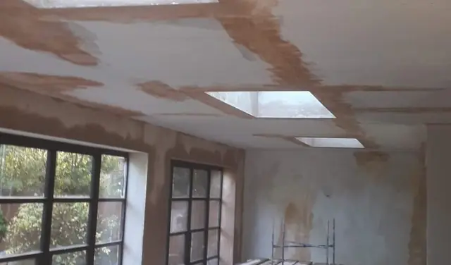 Ceiling with three roof lights in Marlow part-way through skimming, above a wall of black-framed windows